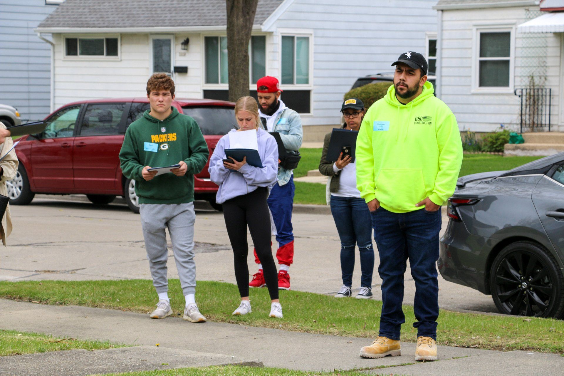 A group of people are standing on the sidewalk in front of a car.