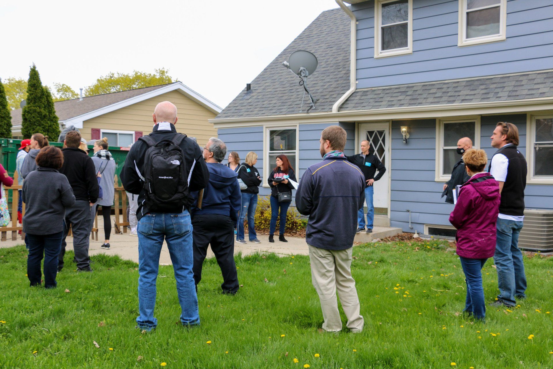 A group of people are standing in front of a blue house.