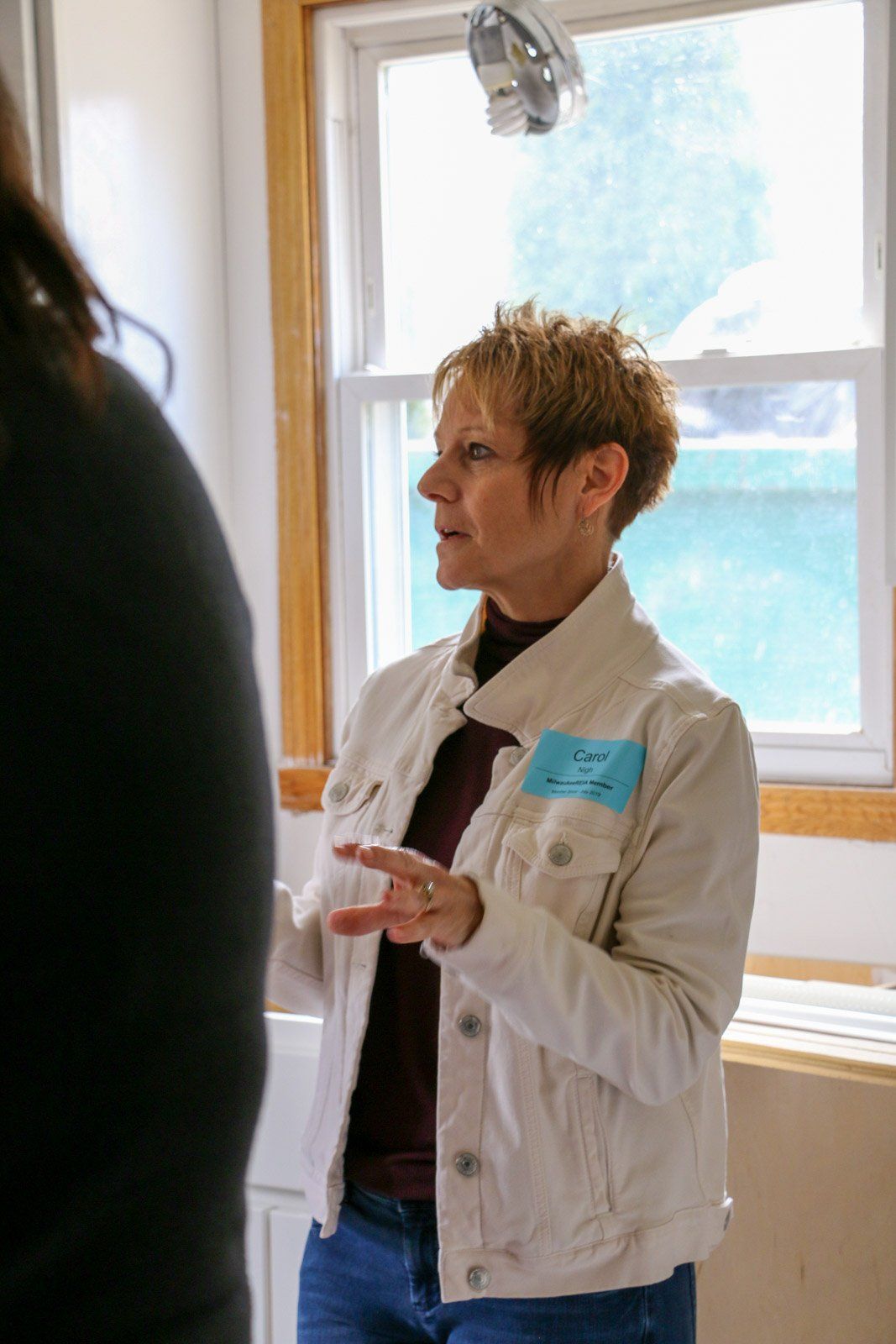 A woman in a white jacket is talking to another woman in front of a window.