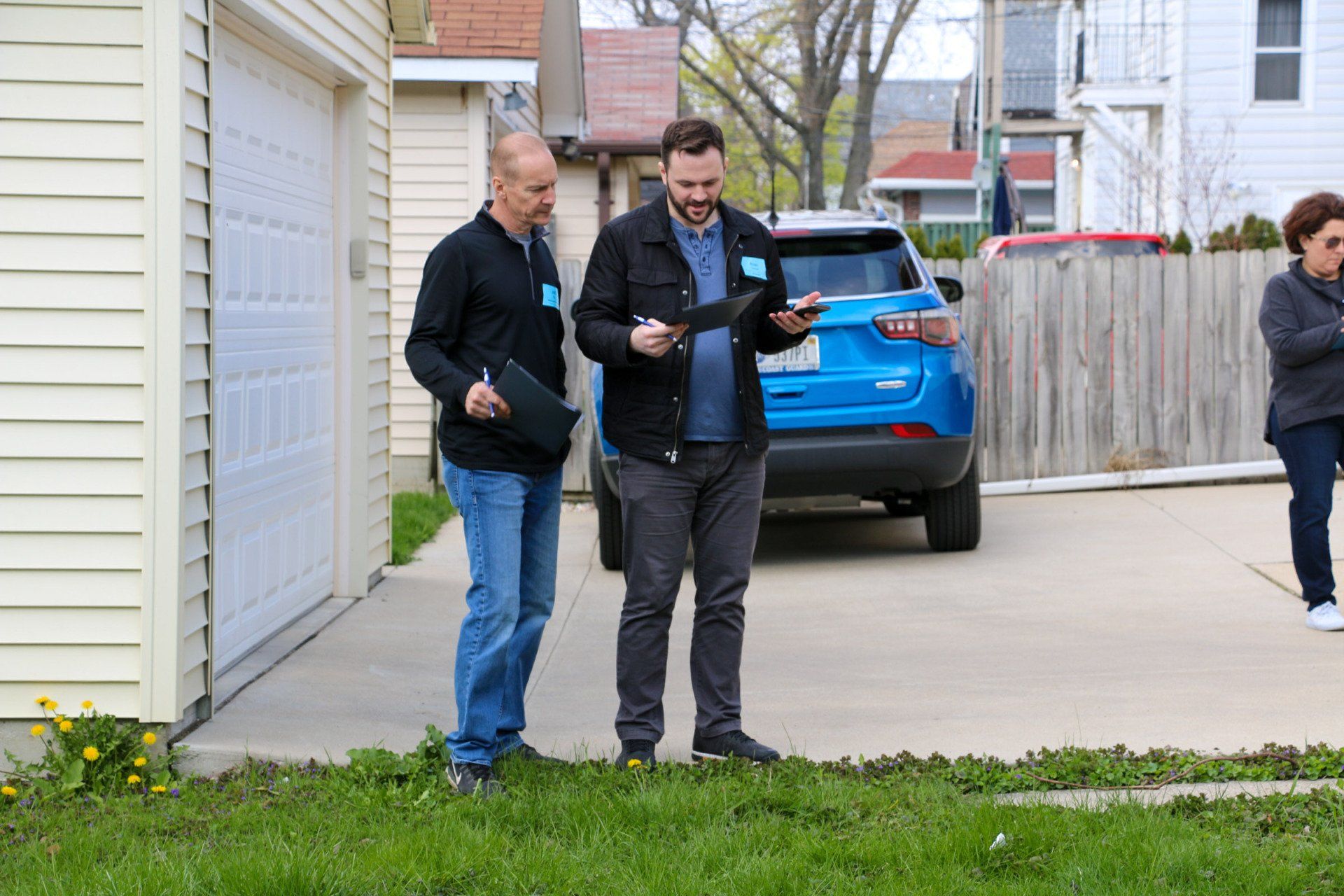 Two men are standing in front of a house looking at a tablet.