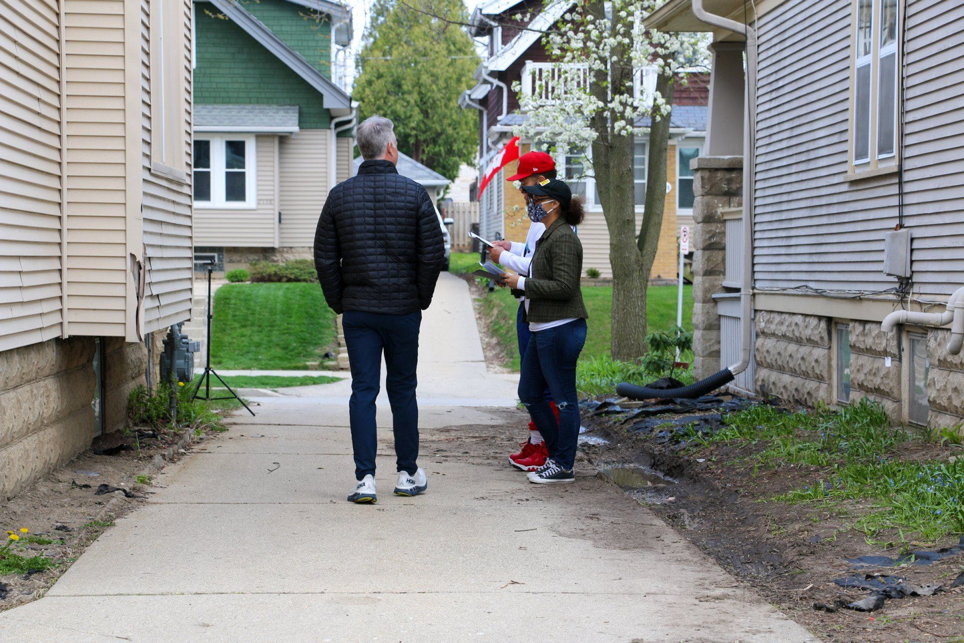 A man and a woman are walking down a sidewalk between two houses.