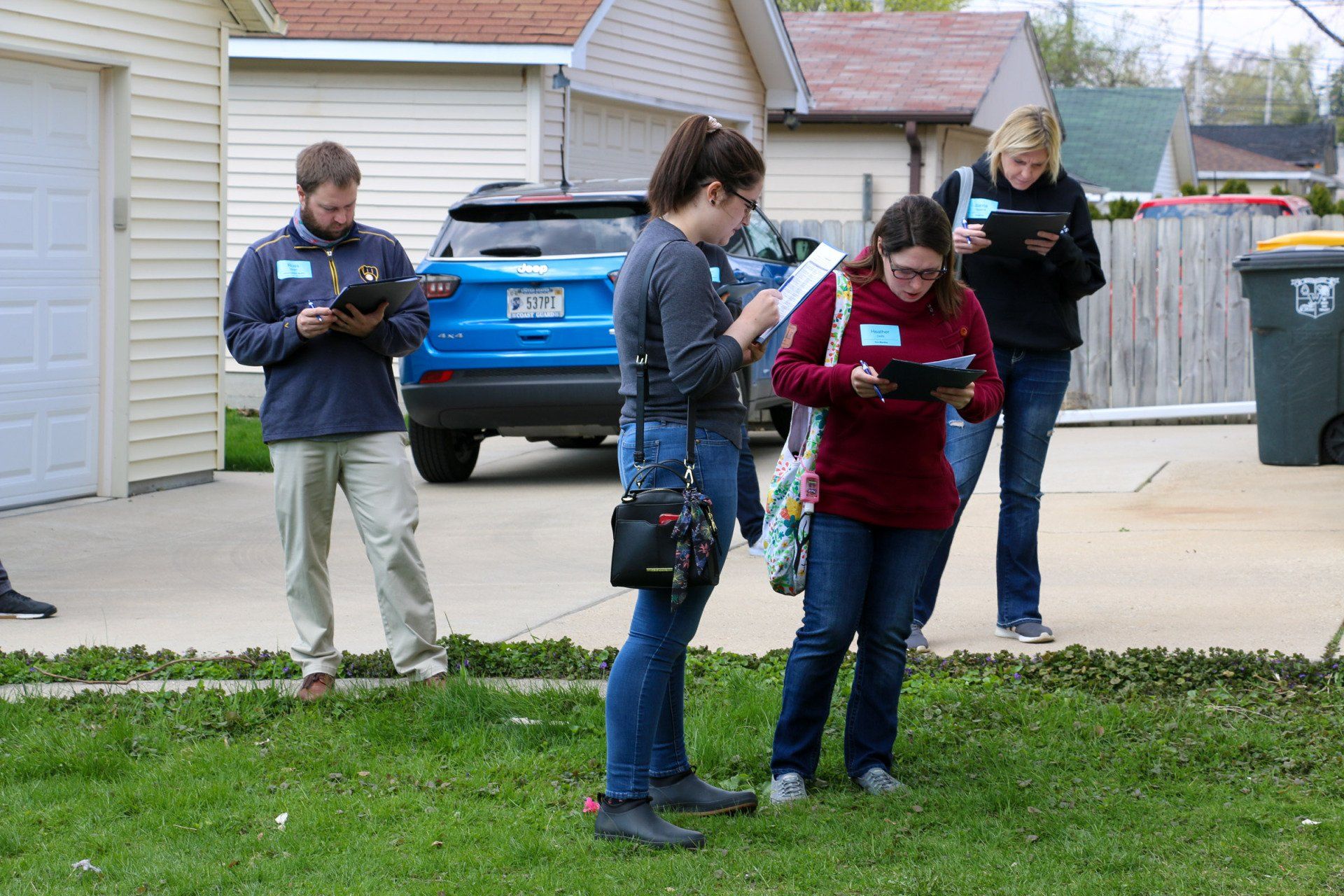 A group of people are standing in front of a house looking at their phones.