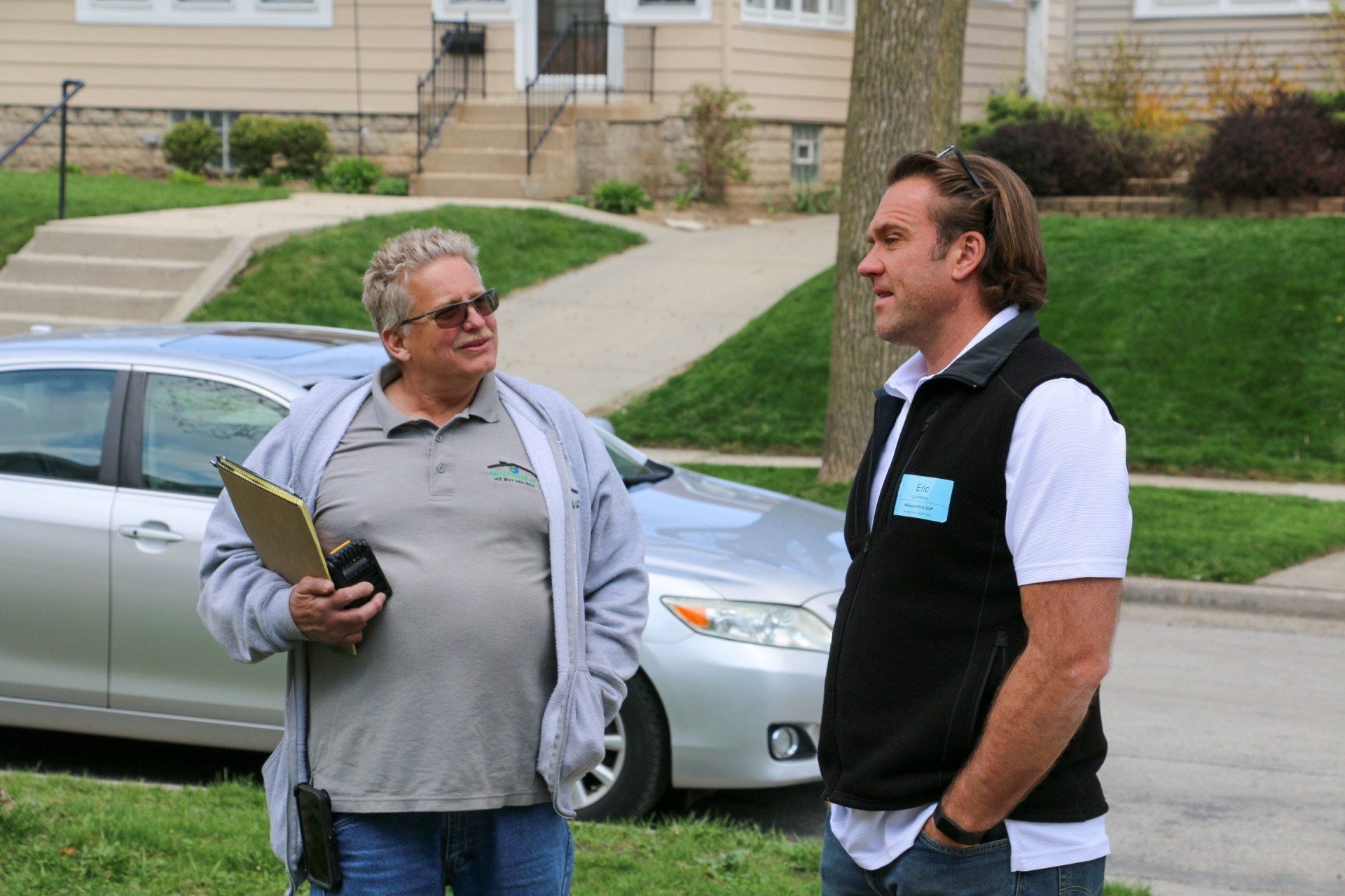 Two men are standing next to each other in front of a silver car.
