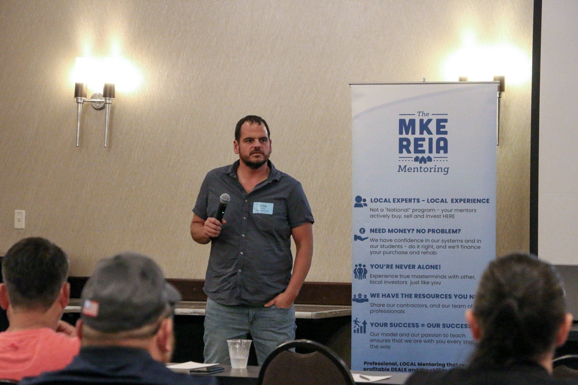 A man is giving a presentation in front of a banner that says mke reia