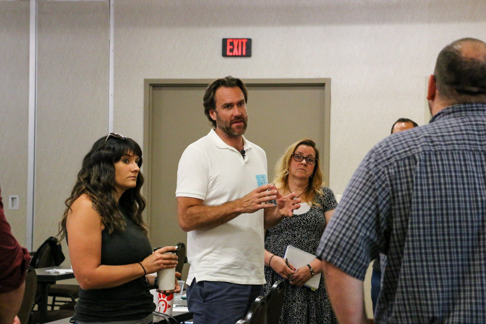A man is talking to a group of people in front of an exit sign.