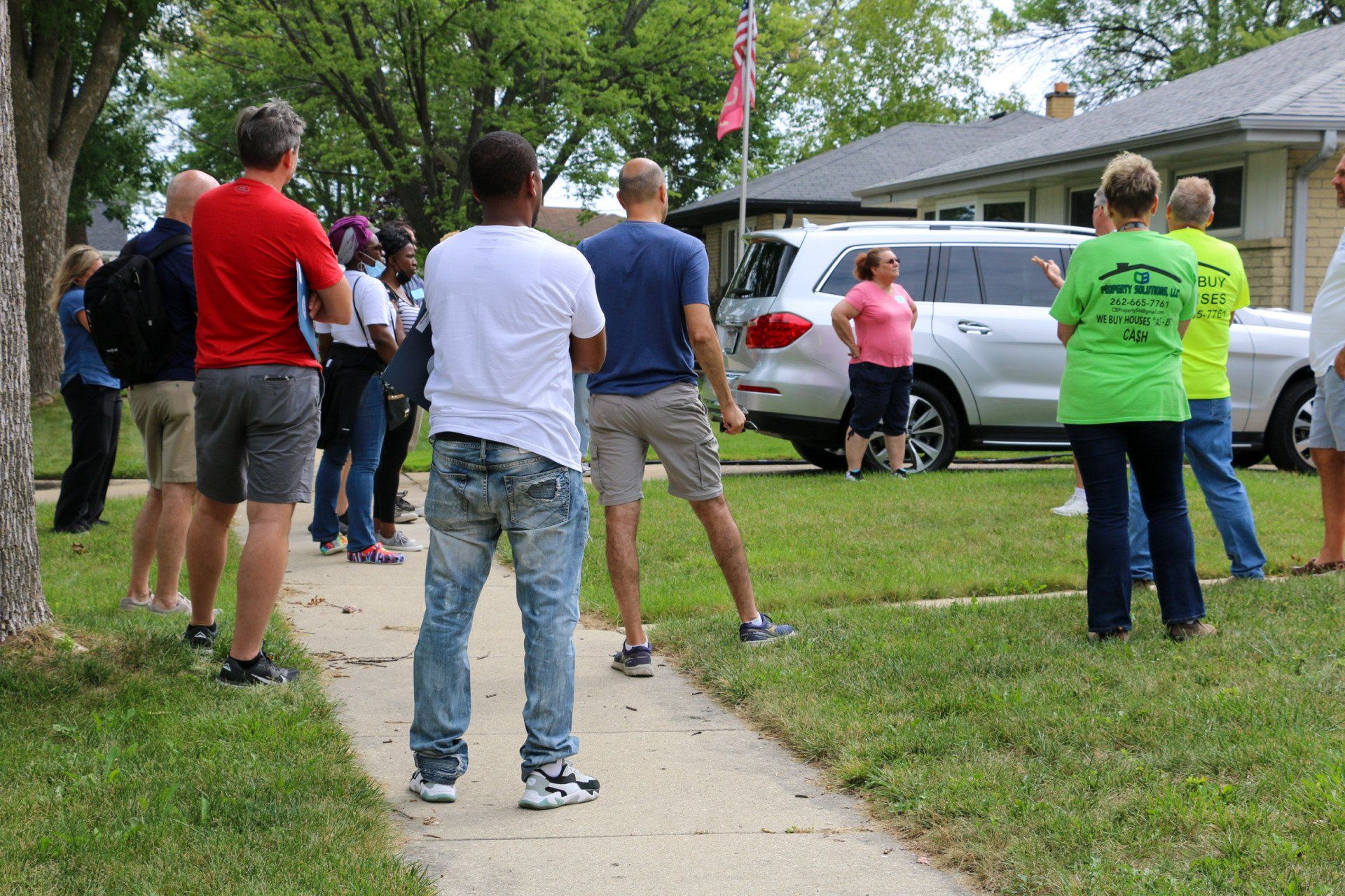 A group of people are standing on a sidewalk in front of a house.