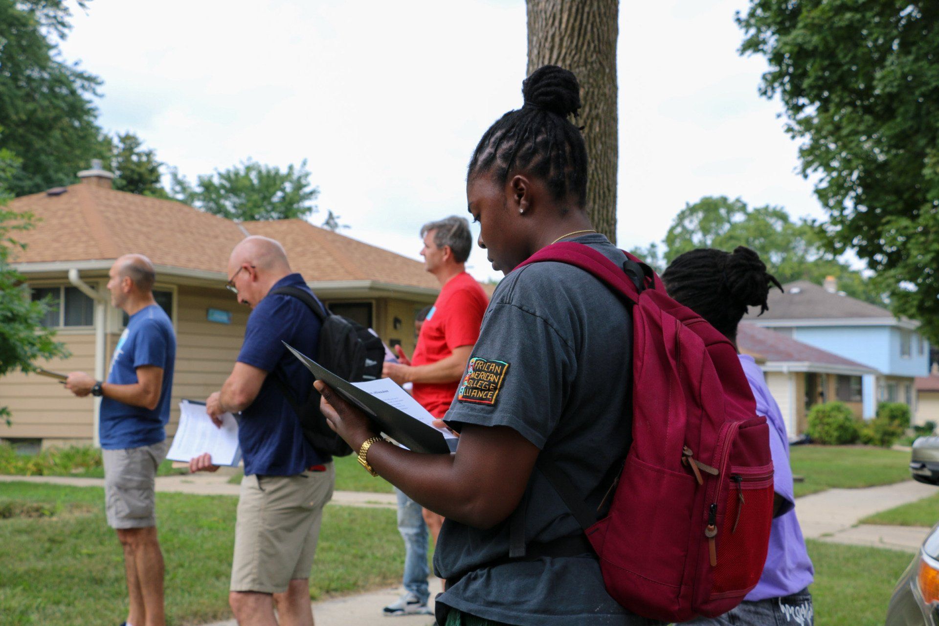 A group of people are standing outside of a house looking at a clipboard.