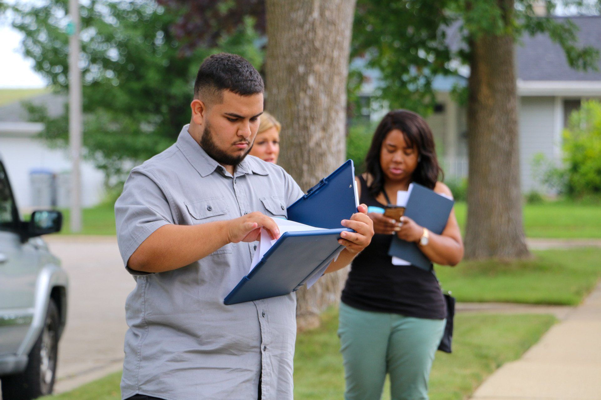 A man and a woman are standing on a sidewalk looking at a clipboard.