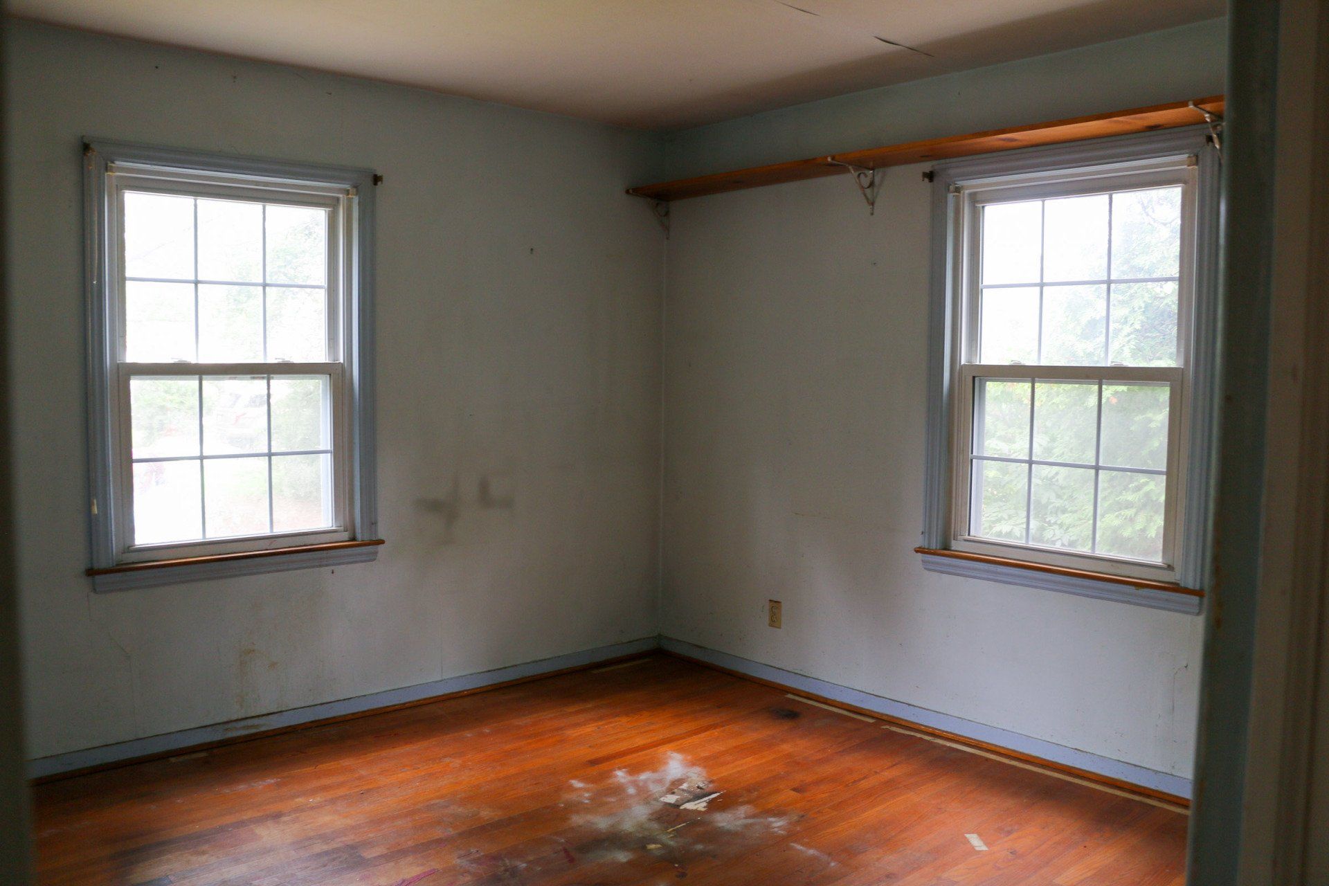 An empty room with two windows and a wooden floor.