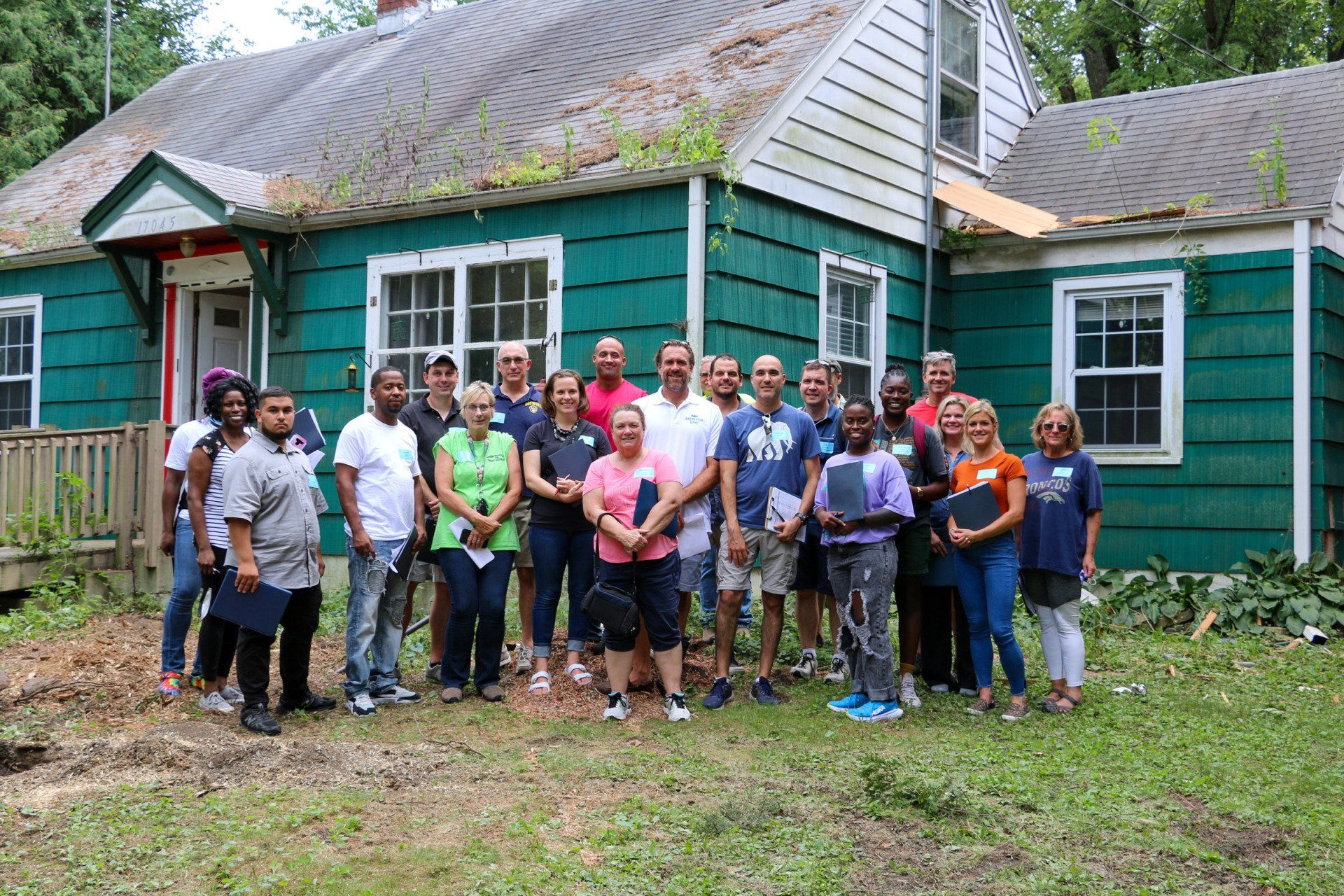 A group of people are posing for a picture in front of a green house.