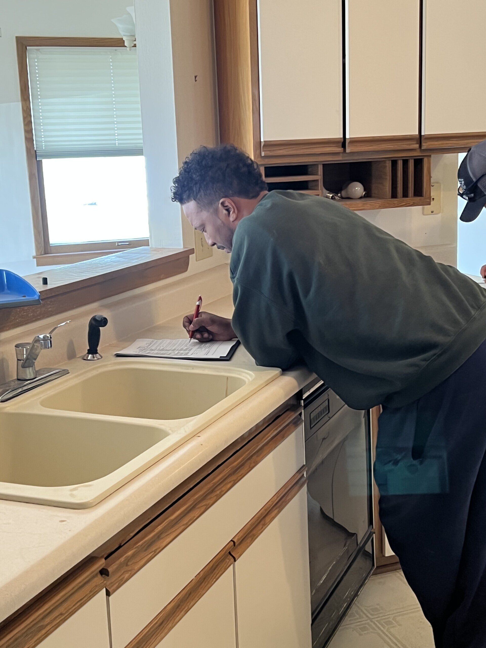A man is writing on a clipboard in a kitchen