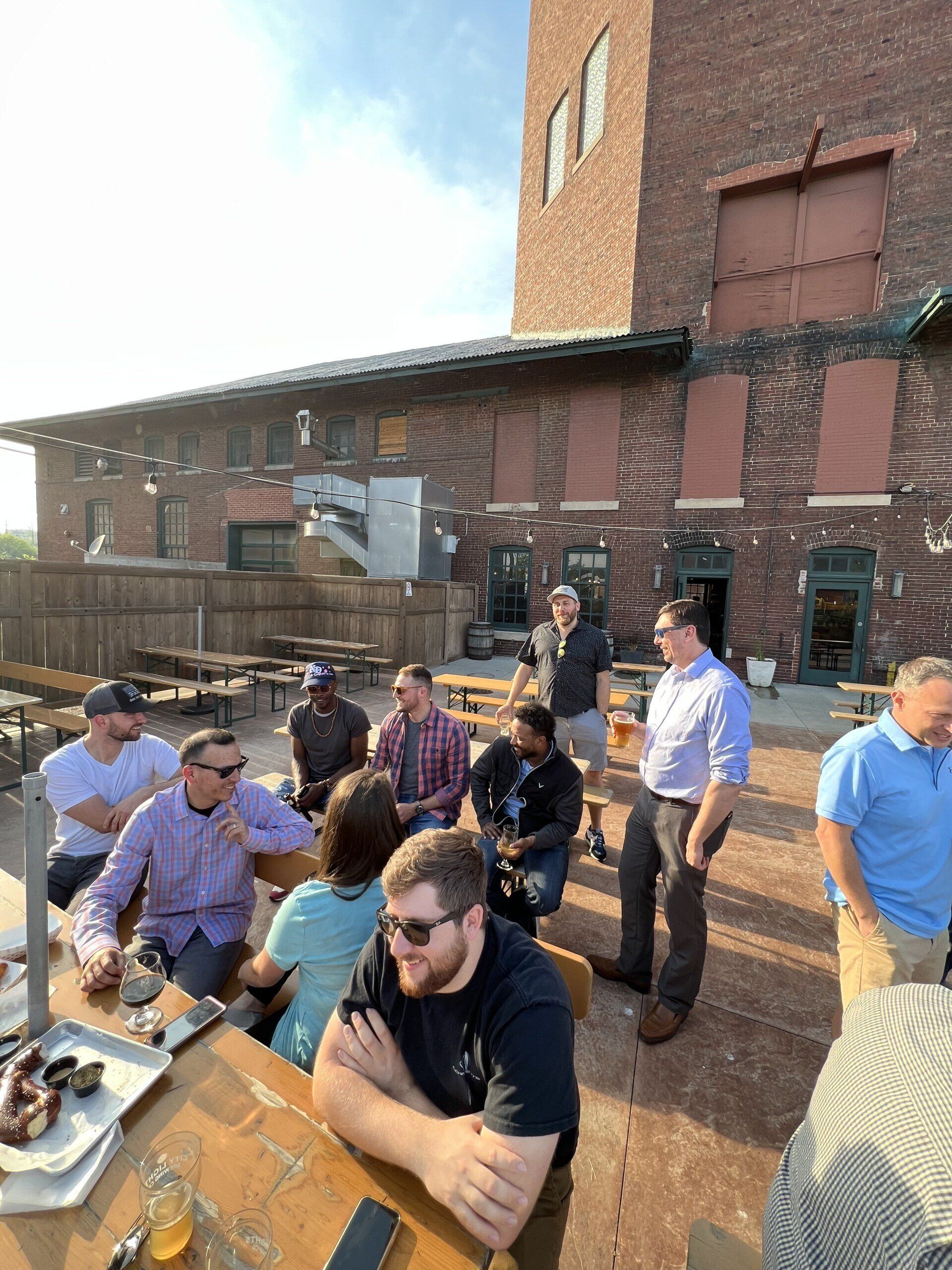 A group of men are sitting at a table in front of a brick building.