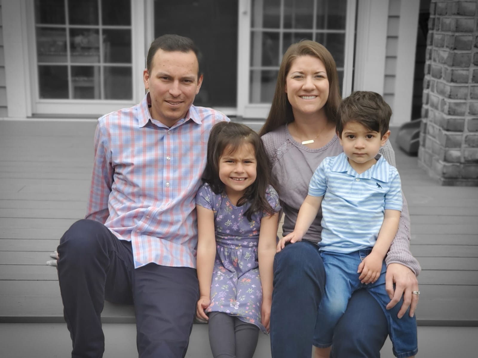 A family is sitting on a porch posing for a picture.