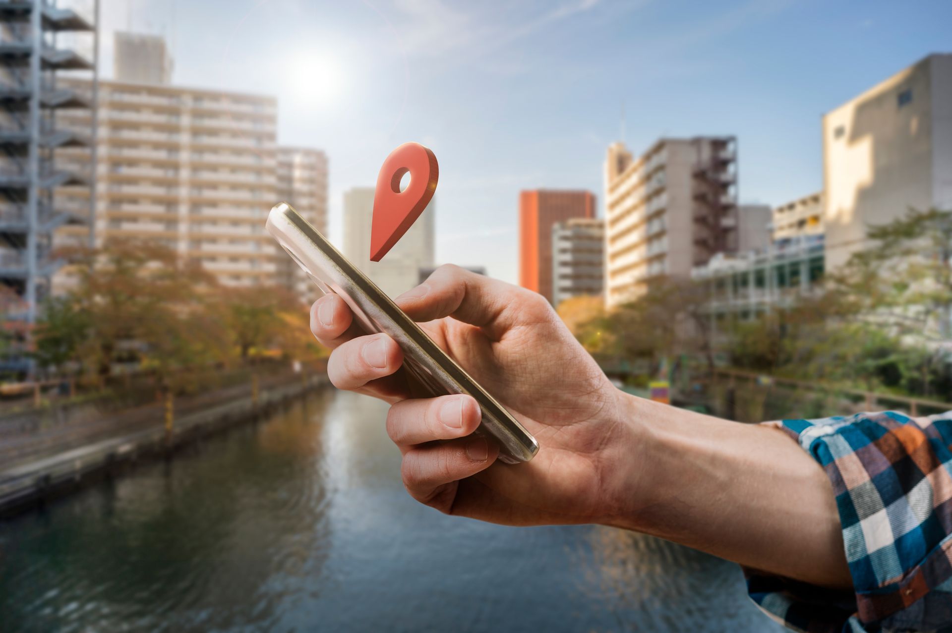 Man holding phone with red location tag image above it and a downtown riverwalk in the background