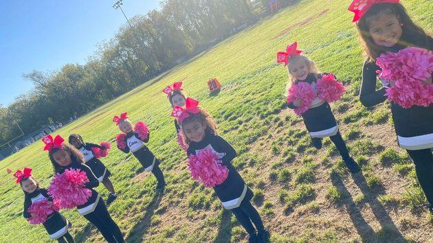 Cheerleader in red uniform performs a backbend on a green and red football field.