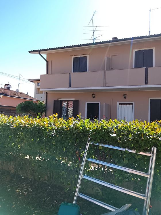 Casa beige a due piani dietro una siepe verde, con una scala di metallo appoggiata davanti.