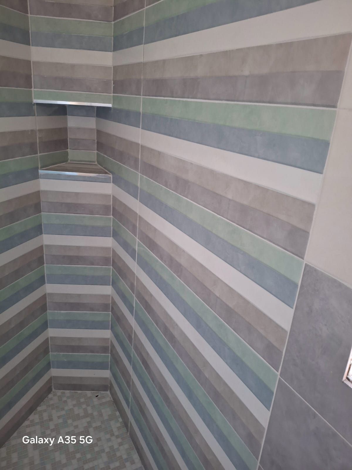Angolo di una parete della doccia o del bagno rivestito con piastrelle a righe grigie, blu e bianche.