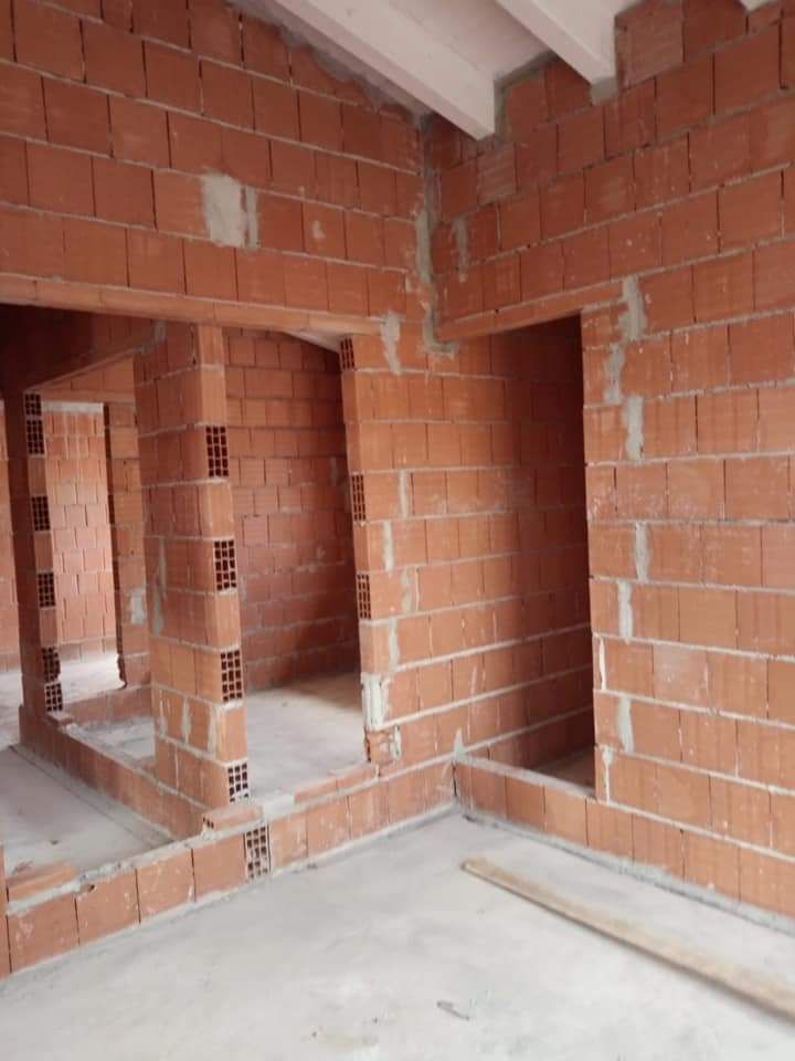 Interno in mattoni non rifinito con nicchie, aperture per porte e pavimento in cemento in fase di costruzione.