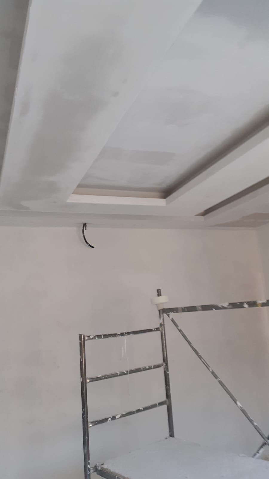 Stanza parzialmente rifinita con controsoffitto bianco, fili elettrici a vista e una scala metallica appoggiata al muro.