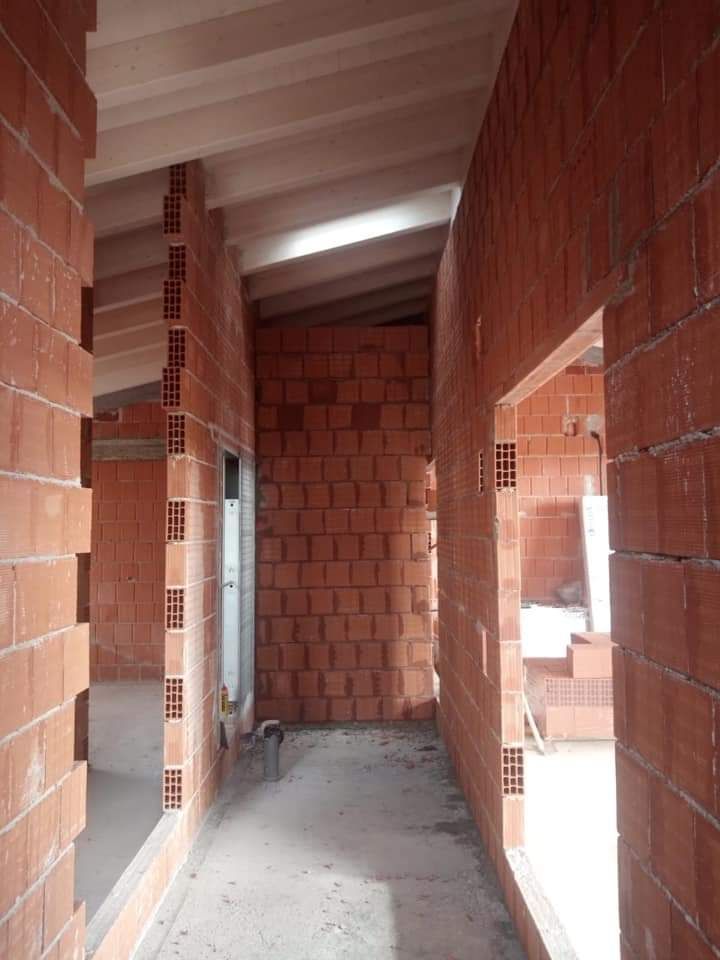 Corridoio in mattoni non rifinito con porte aperte e pavimento in cemento all'interno di un edificio in costruzione