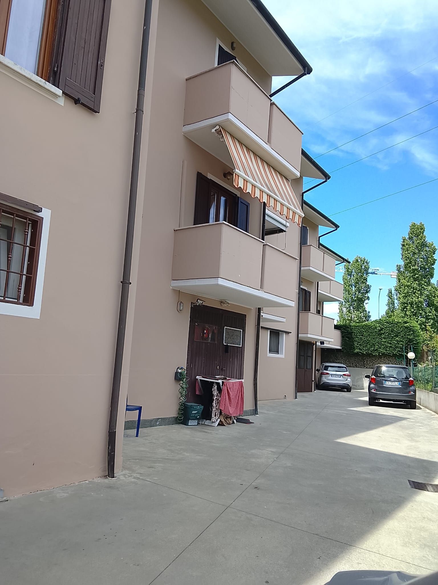 Cortile di un condominio con auto parcheggiate, balconi e un vialetto soleggiato sotto un cielo azzurro.
