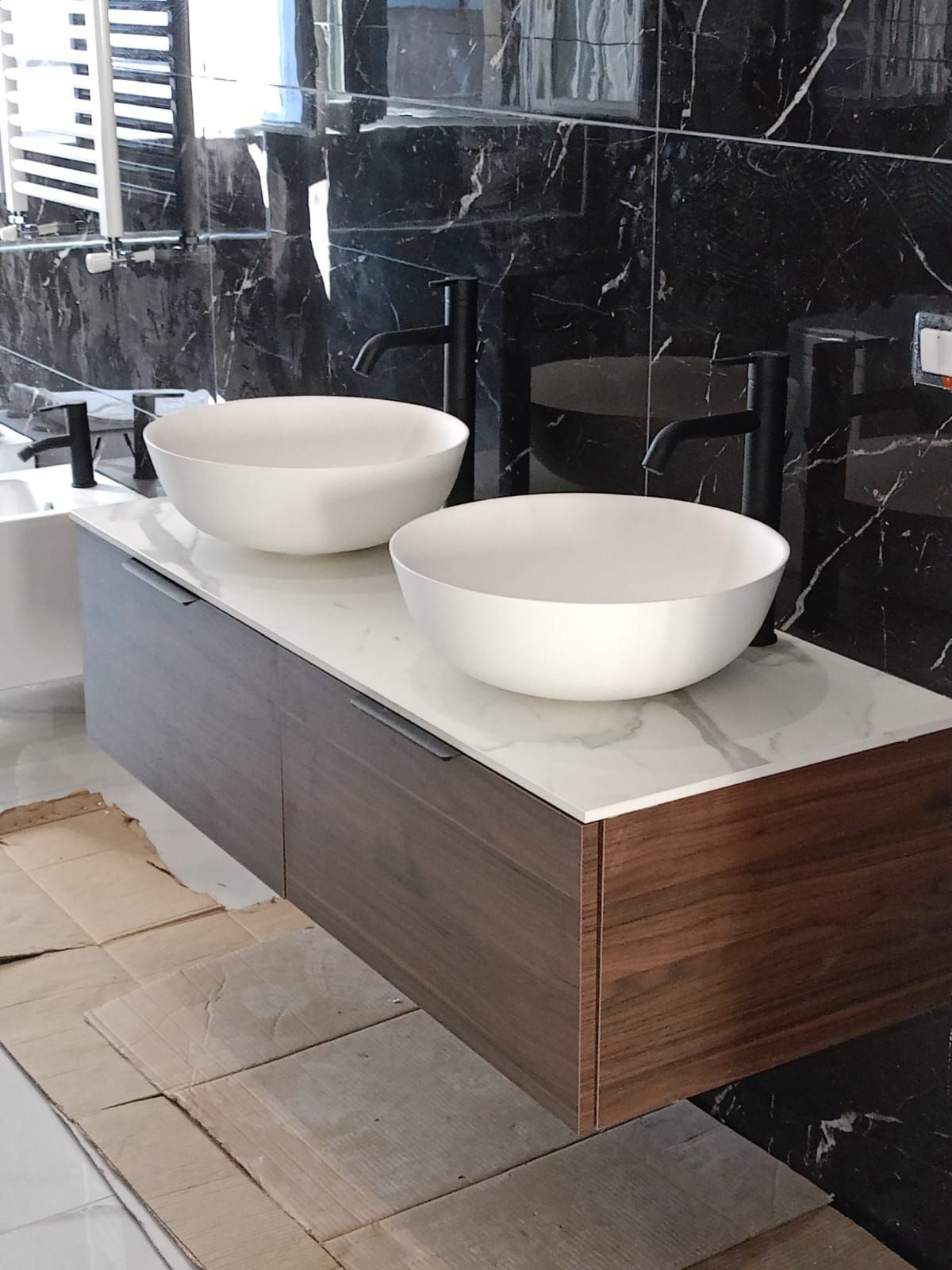 Mobile bagno moderno con due lavabi a ciotola bianchi su piano in legno, addossati a pareti in marmo scuro.