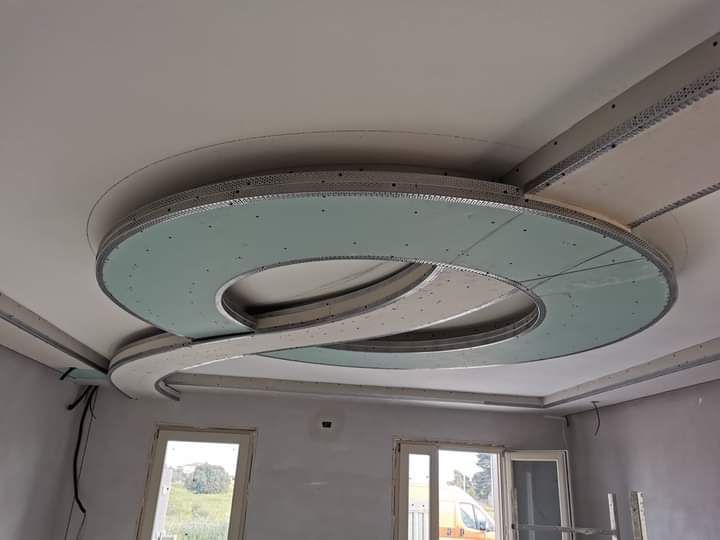 Grande lampadario circolare a soffitto con anello verde menta in una stanza in fase di ristrutturazione.