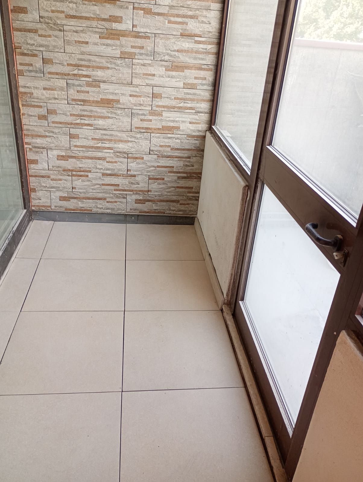 Piccolo balcone piastrellato con parete effetto pietra e porte scorrevoli in vetro satinato.