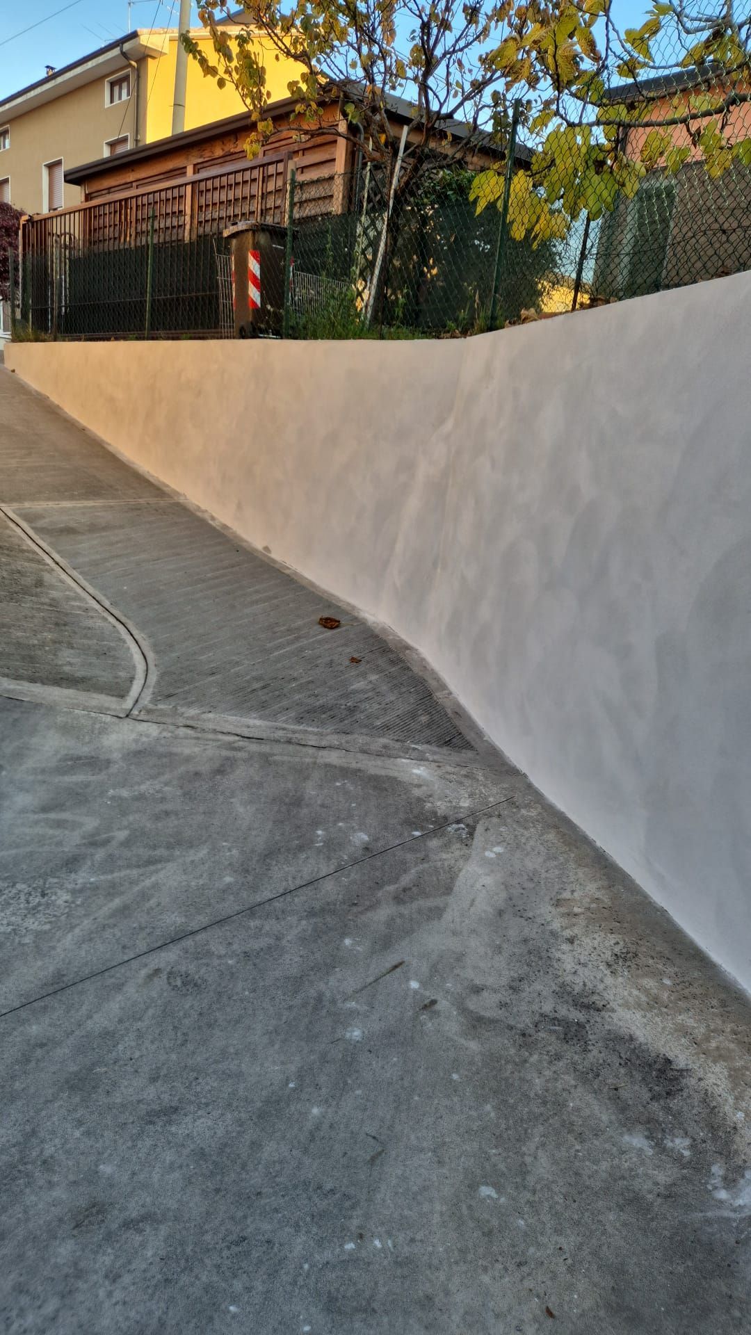 Vialetto curvo in cemento accanto a un muro di contenimento bianco e a un edificio giallo nella calda luce del tramonto.