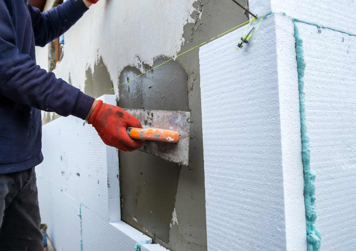 Tetto di tegole rosso-marrone in un cantiere edile, con mattoni accatastati e pali della luce sullo sfondo.