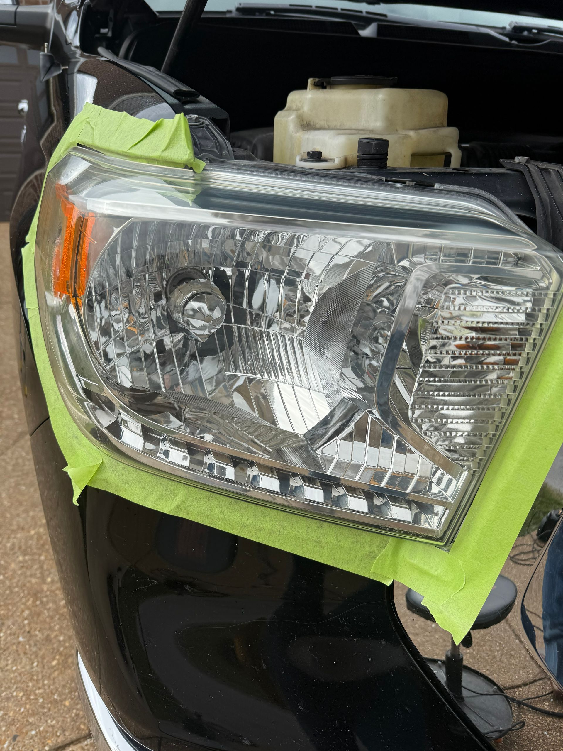 Close-up of a red car’s front headlight and fender, with the hood open.