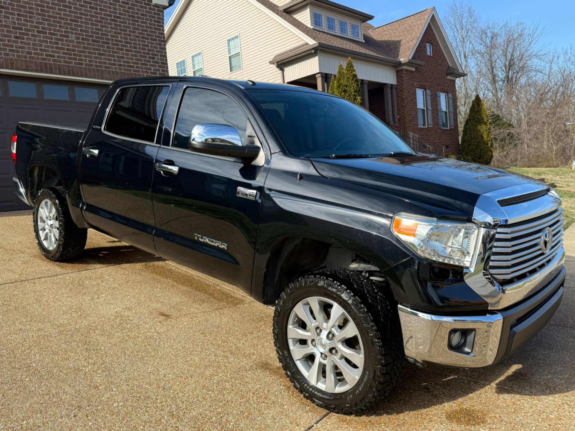 Black pickup truck parked in front of a brick house on a sunny day