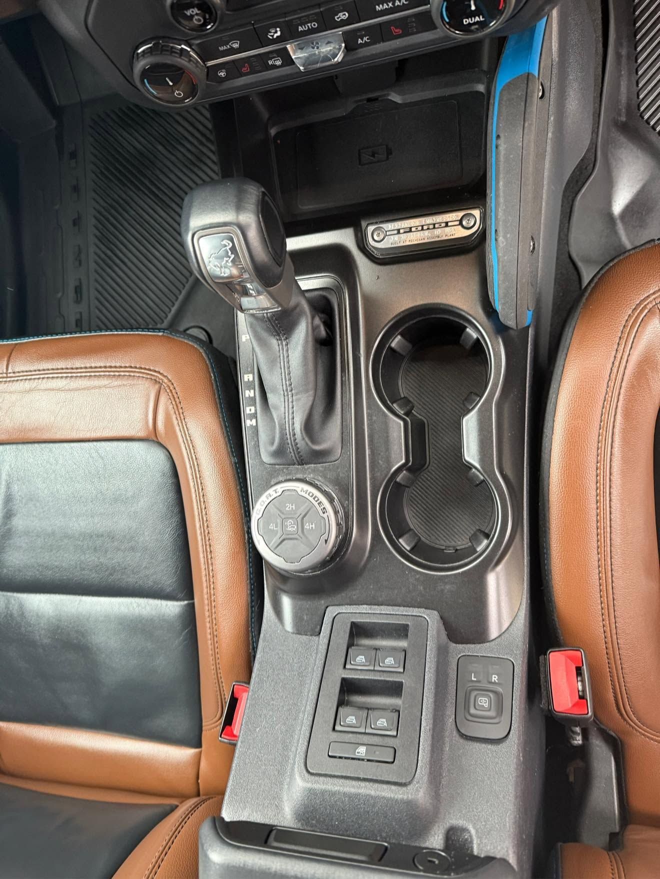 Car interior center console with gear shifter, cup holders, and brown leather seats