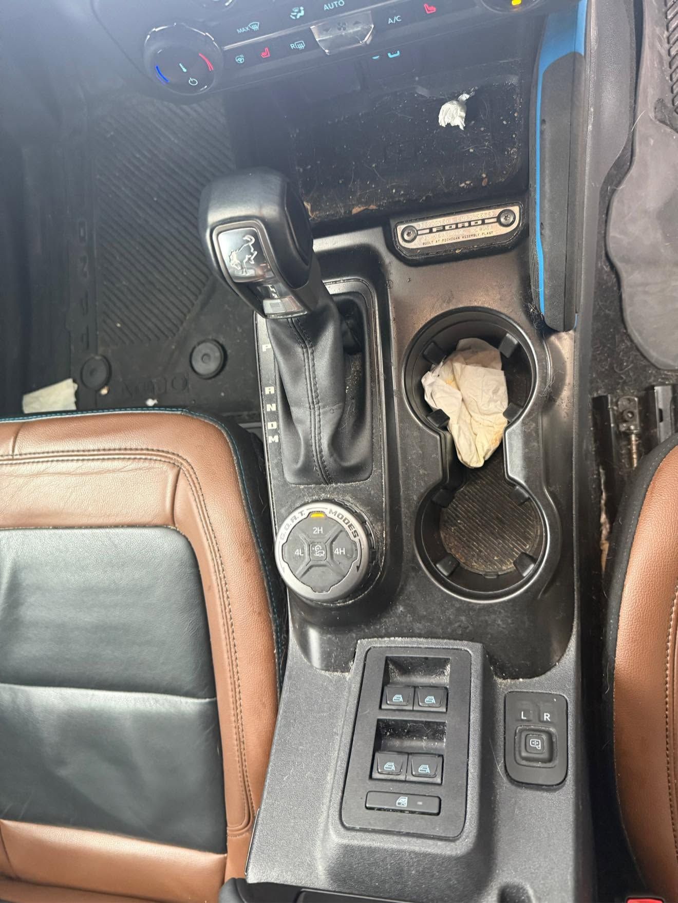 Car center console with gear shifter, cup holders, window controls, and a torn storage compartment exposing contents