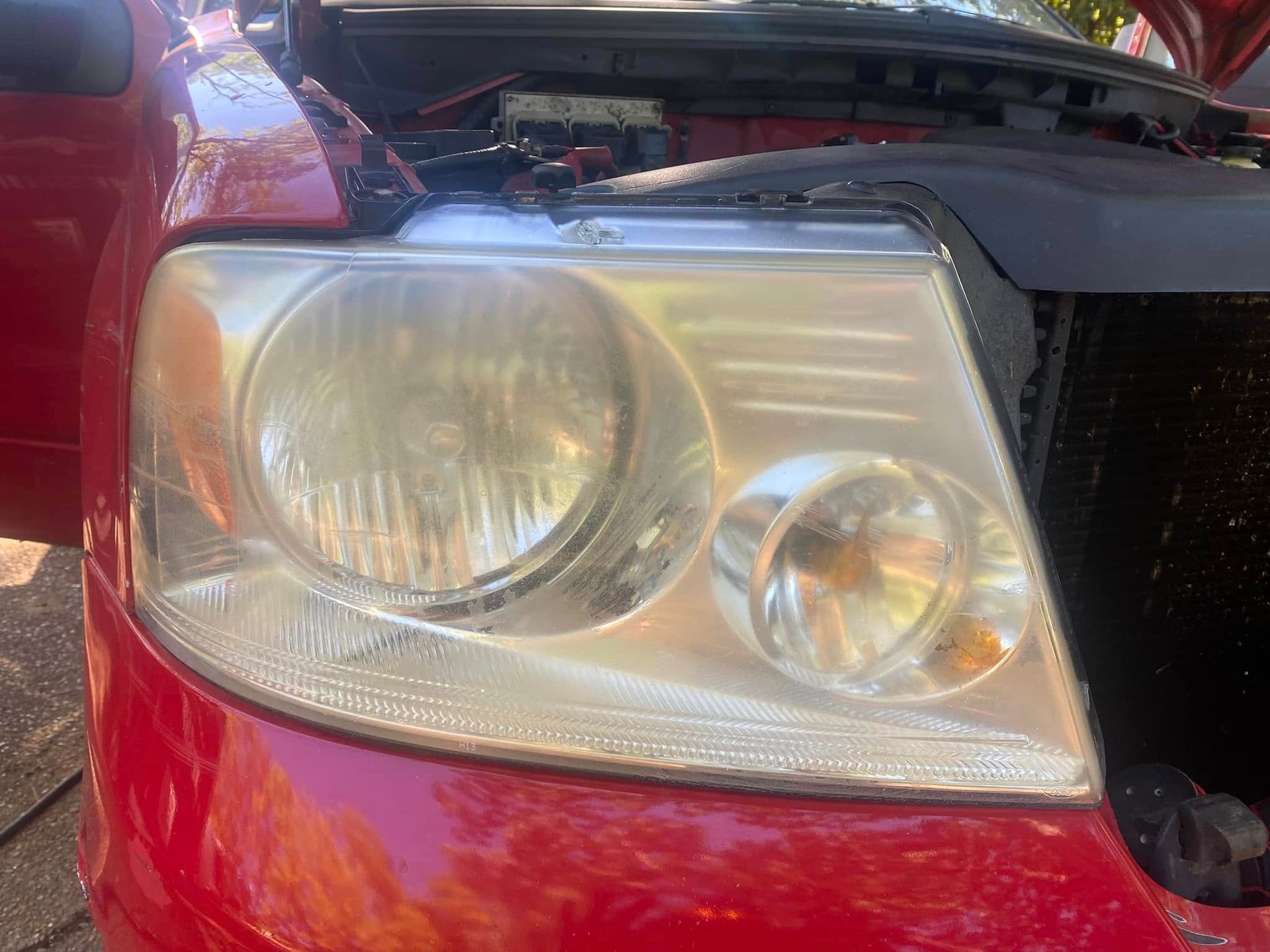 Close-up of a red car’s front headlight with the hood open