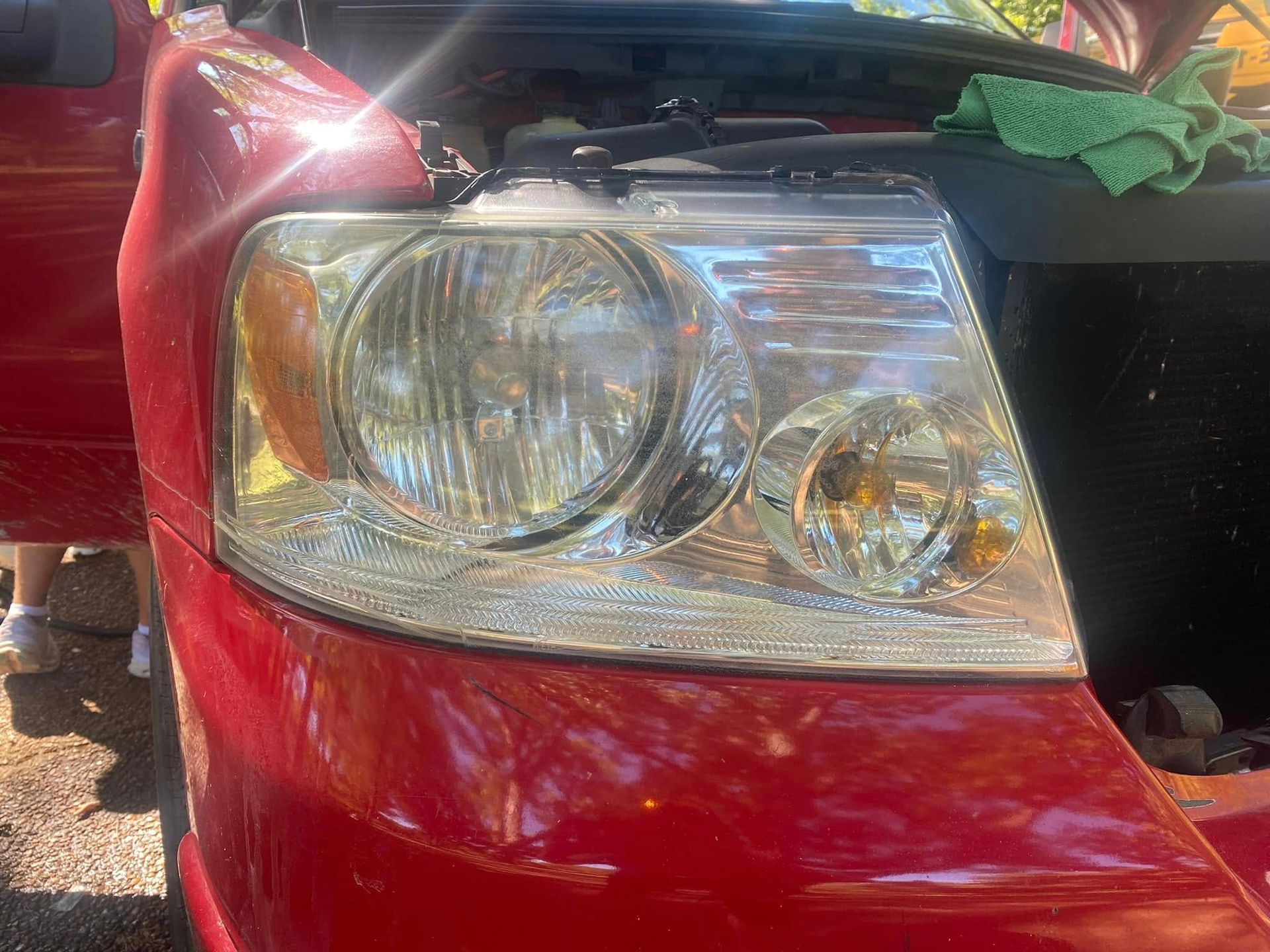 Close-up of a red car’s front headlight and hood with the front end partially open
