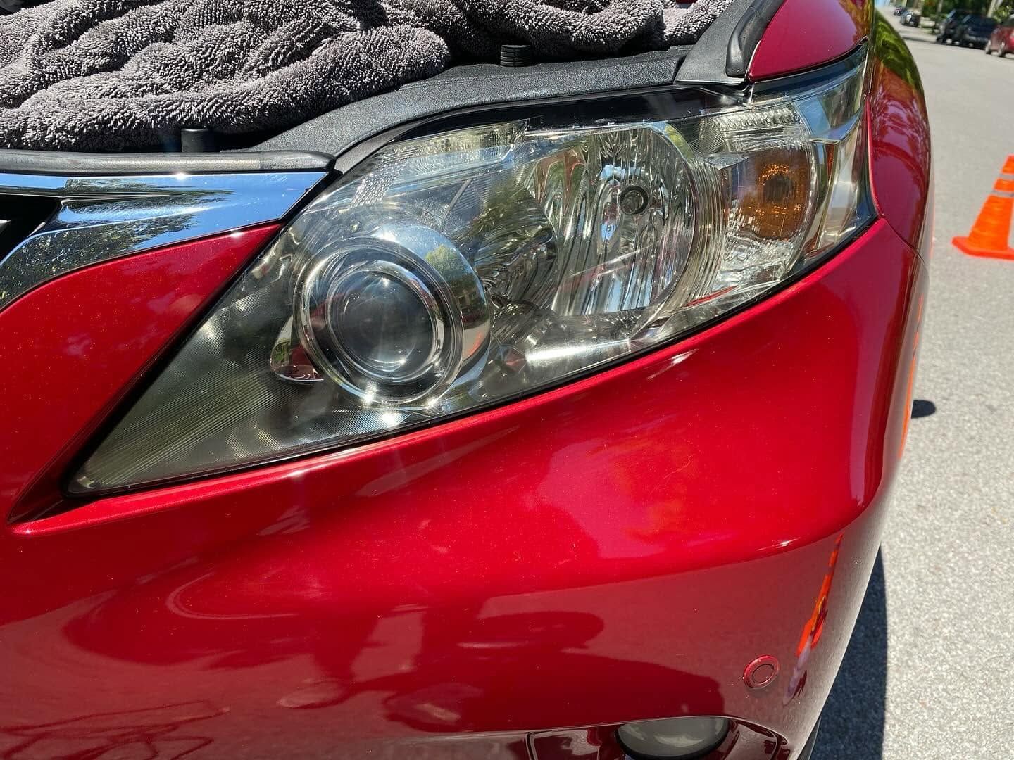 Close-up of a red car front end with a clear headlight and an orange traffic cone nearby