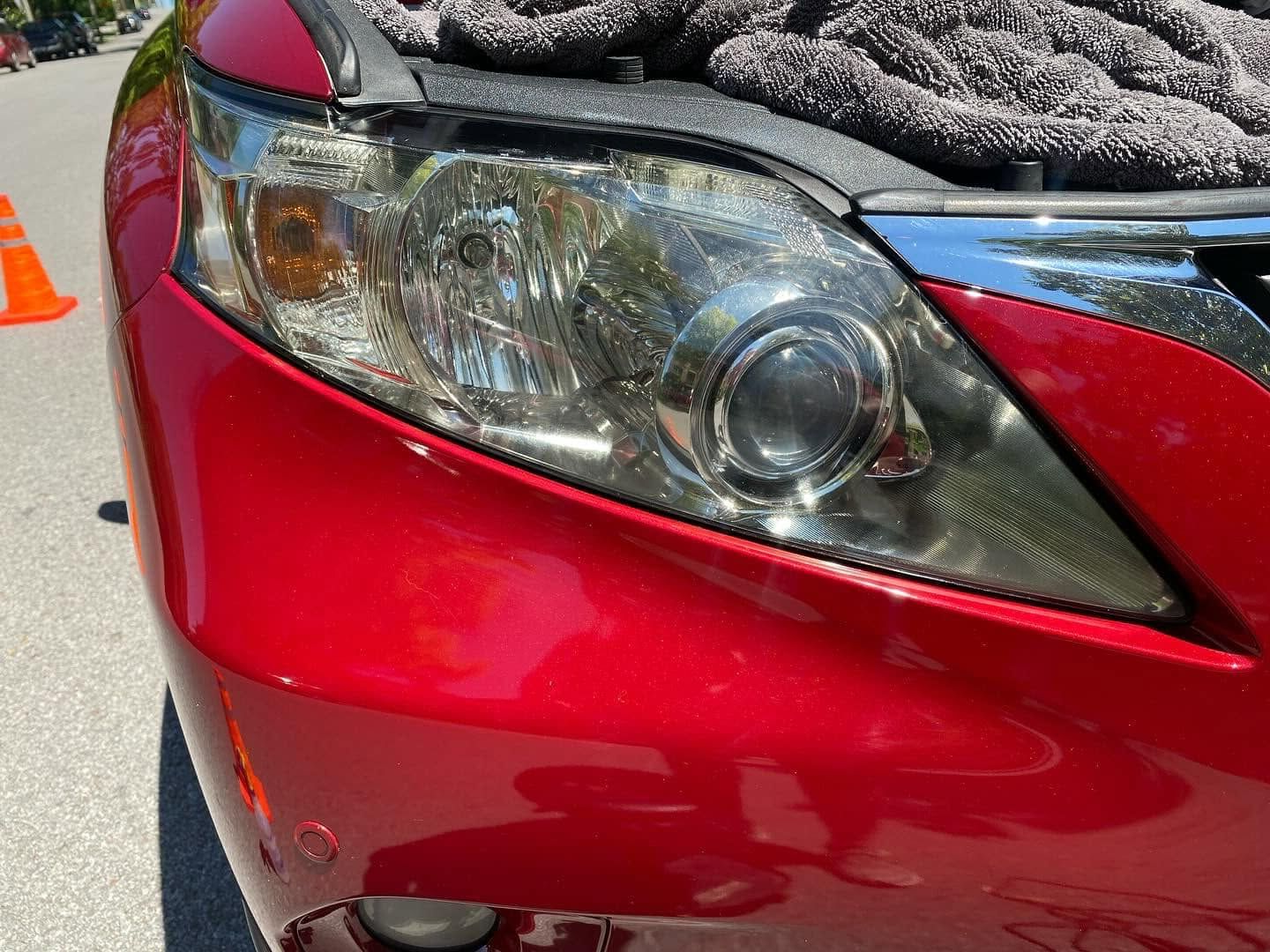 Close-up of a red car’s front headlight and bumper with visible damage and a scuffed hood.