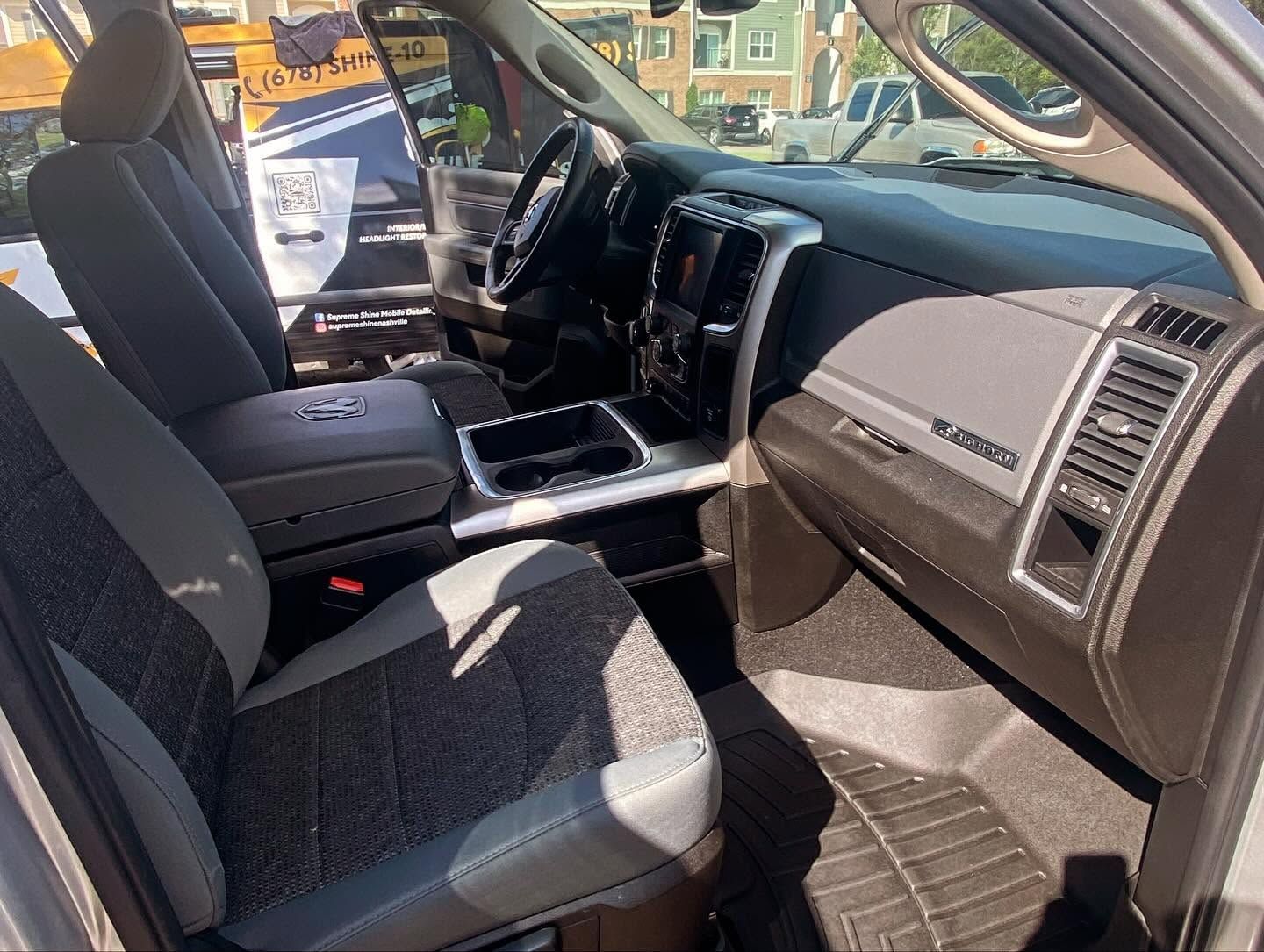 Interior of a pickup truck with gray seats, dashboard, and open passenger door in daylight