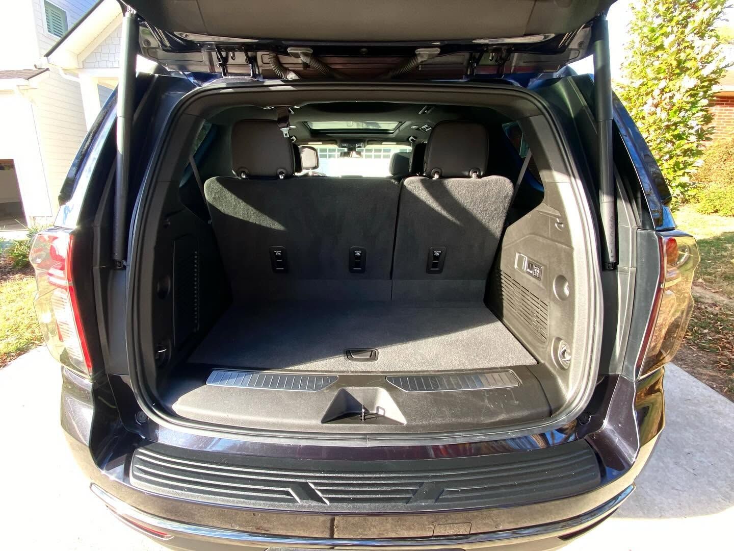 Open SUV cargo area with folded rear seats and black interior, rear hatch raised outside.