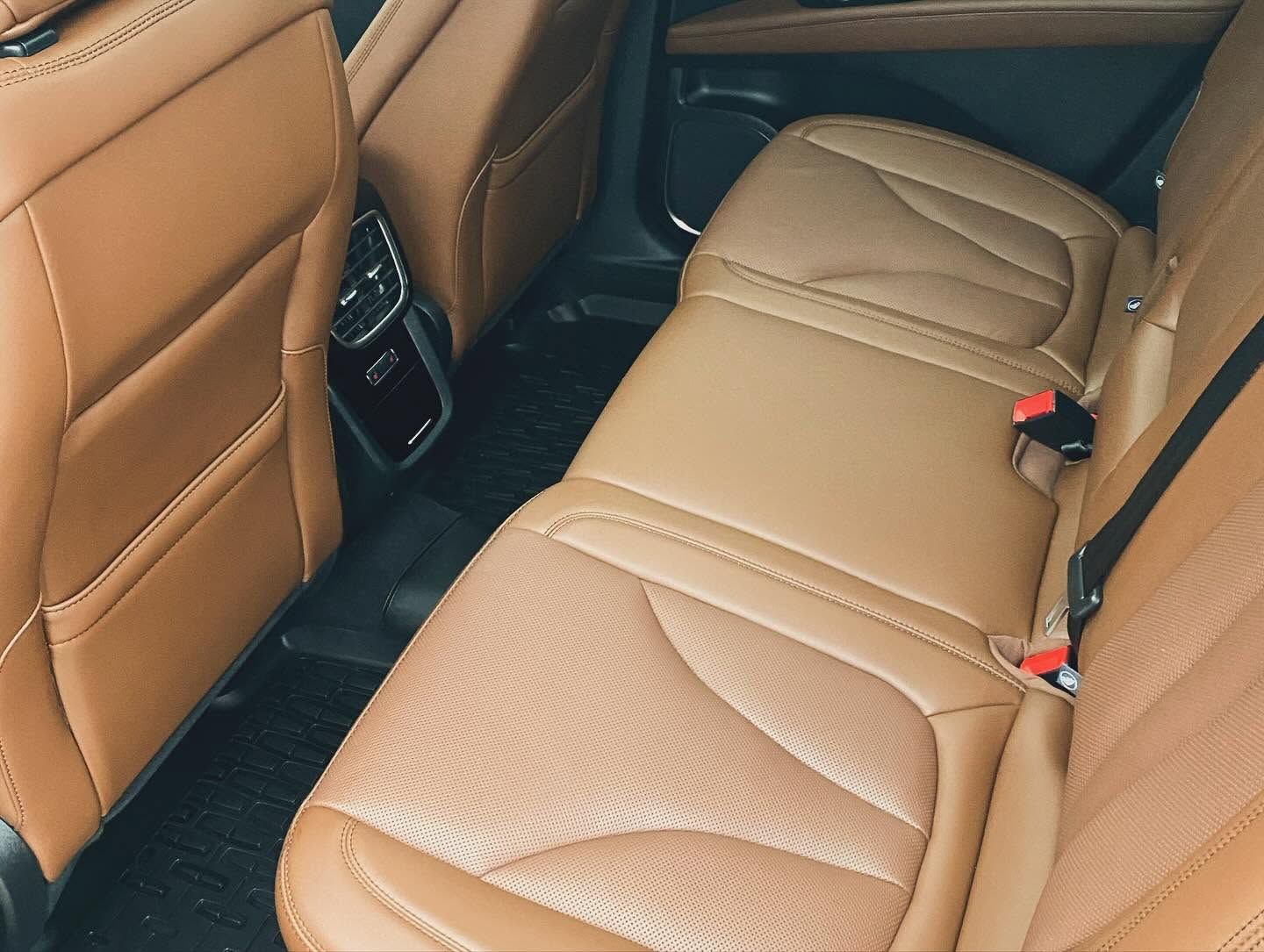 Tan leather car back seat with stitched upholstery and red seatbelt buckles
