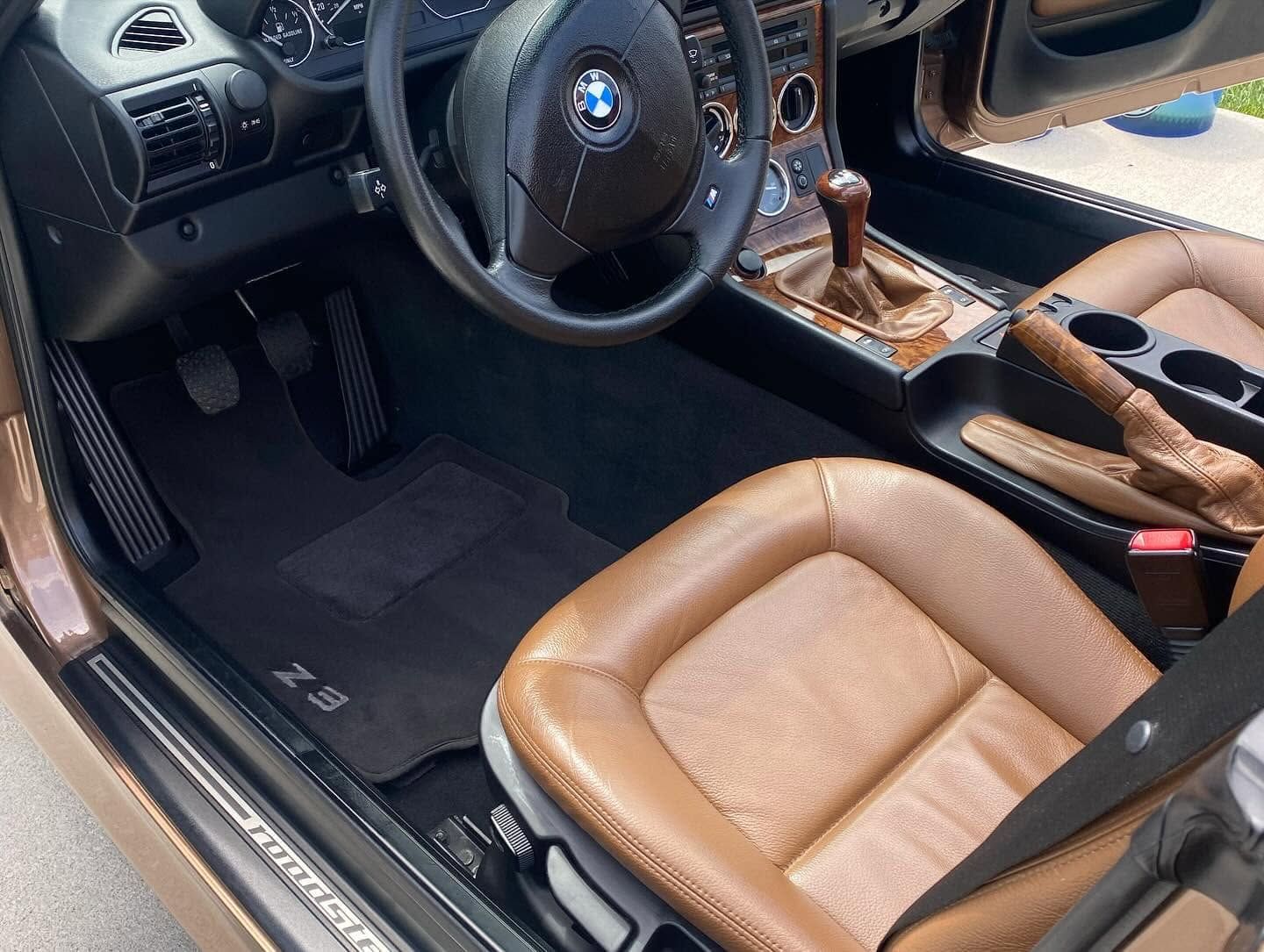 Luxury car interior with tan leather seats, black dashboard, steering wheel, and wood trim center console