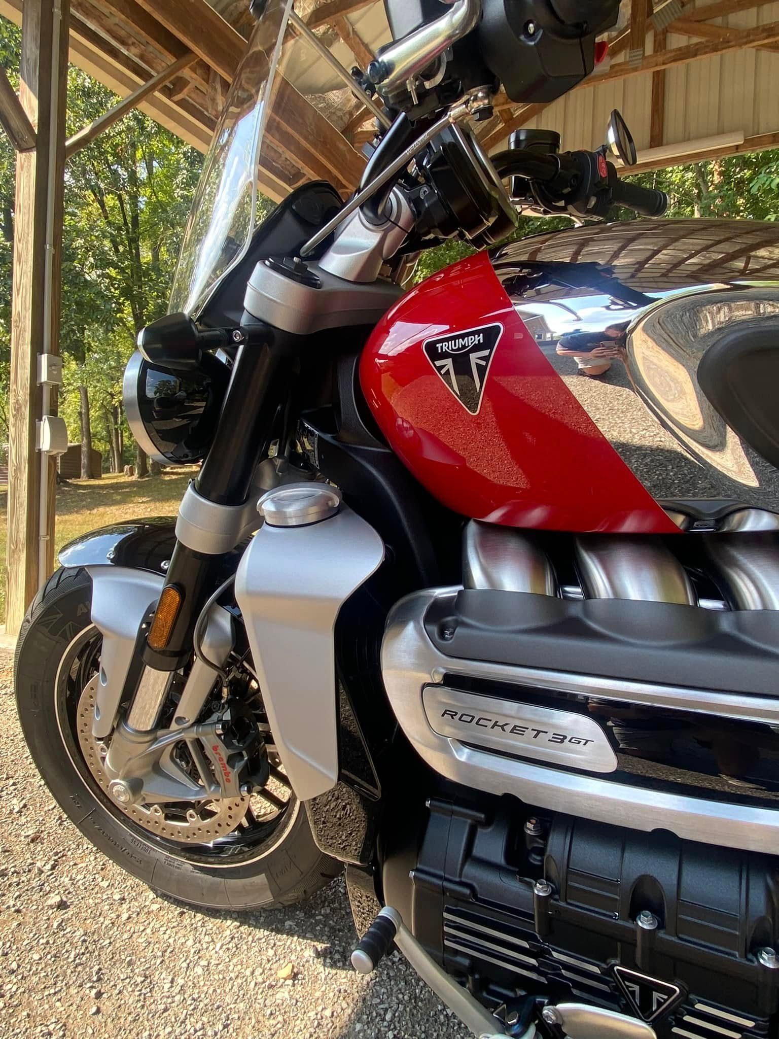 Red and silver motorcycle parked in a wooden carport, close-up of fuel tank and front wheel.