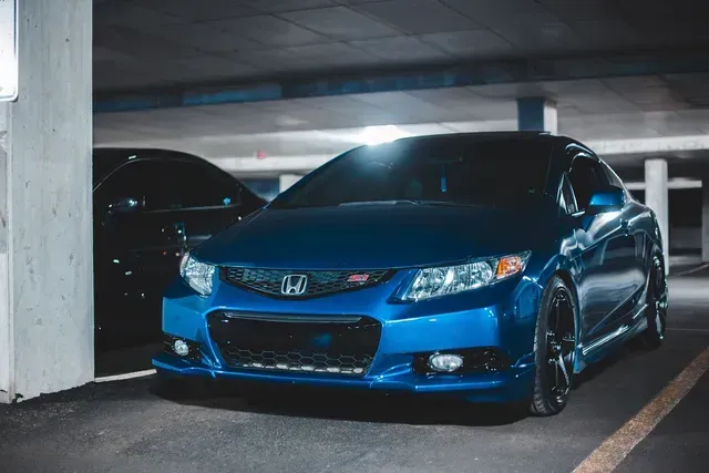 Blue Honda Civic parked in a dim garage, front view with black rims and another car beside it