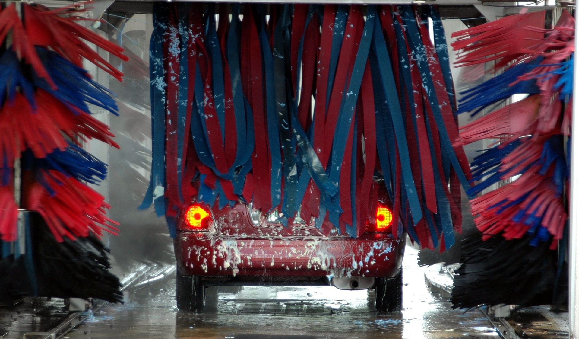 Red car going through a wet automated car wash with blue and red spinning brushes