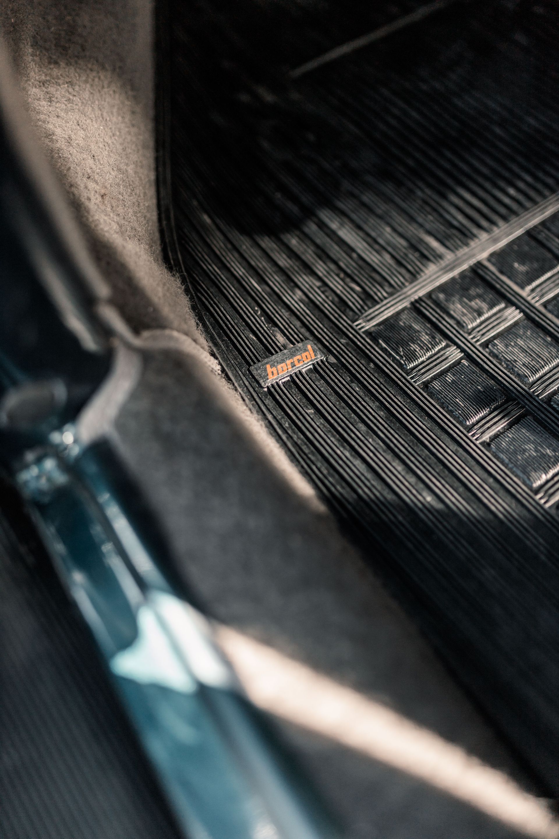 Close-up of a car floor mat and interior door sill with dark textured surfaces and a small brown leaf.