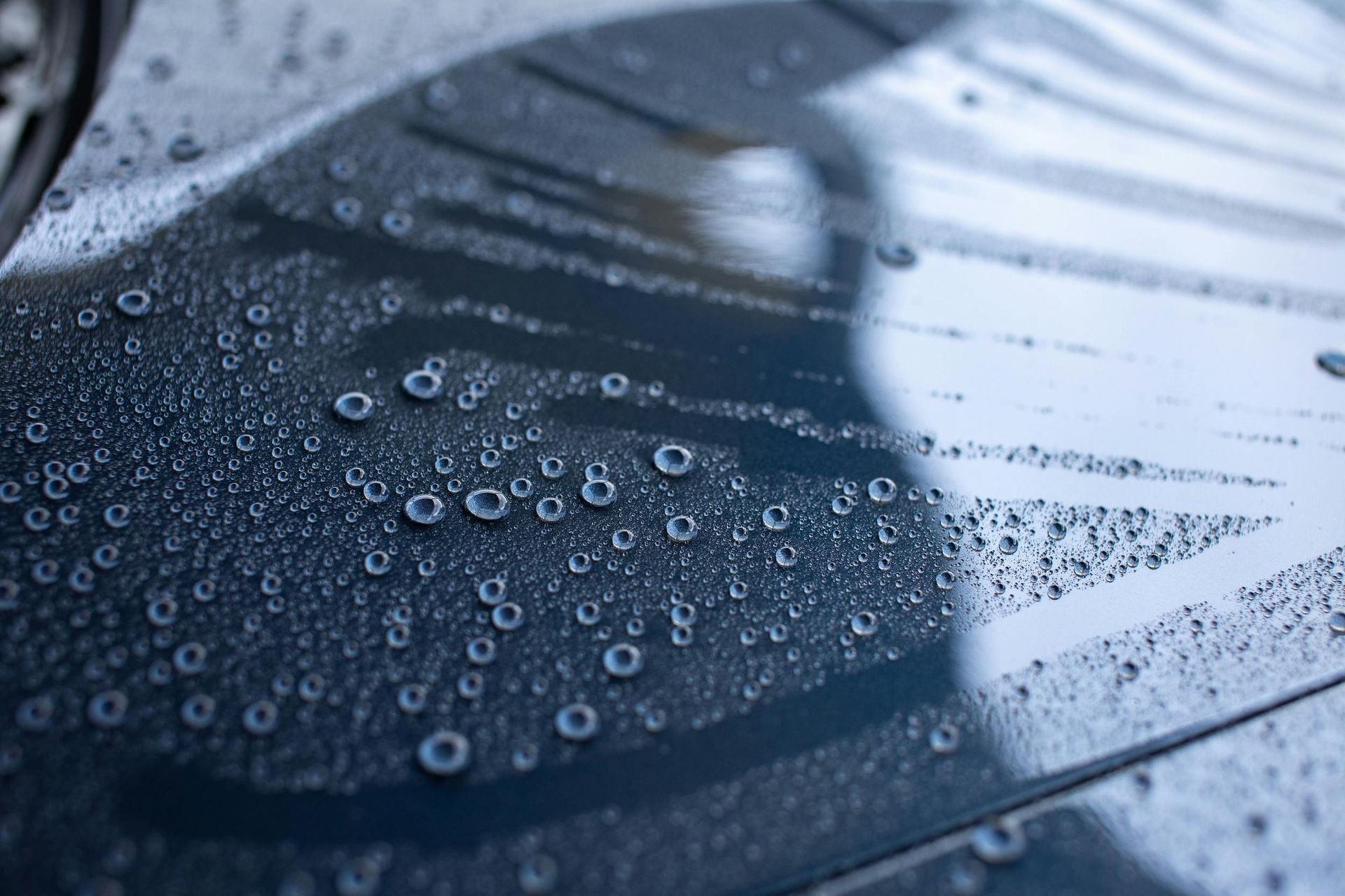 Rain droplets on a dark blue car hood and windshield near a windshield wiper