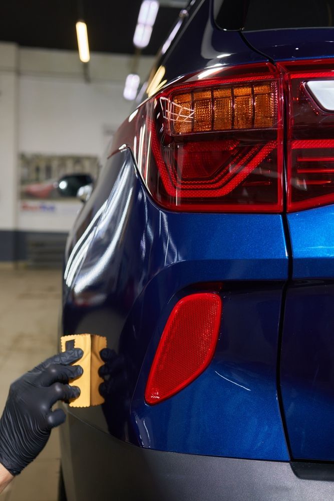 Gloved hand polishing the rear of a blue car with a cloth in a garage