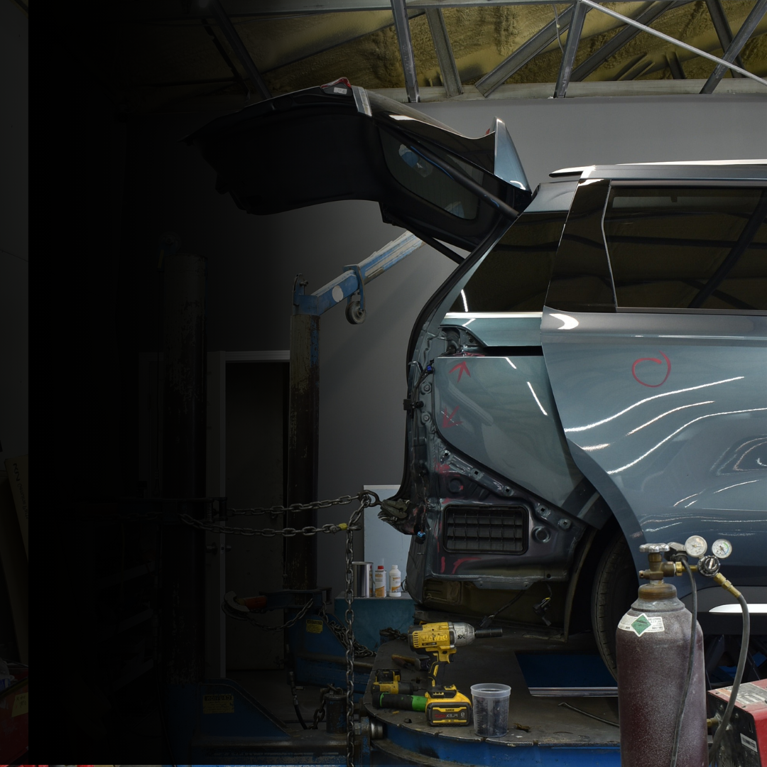 Damaged gray car in an auto body shop with its rear panel open and tools nearby