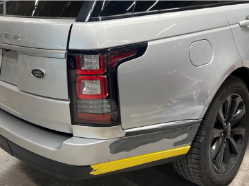 Rear corner of a silver SUV with scrape damage and yellow paint along the lower bumper